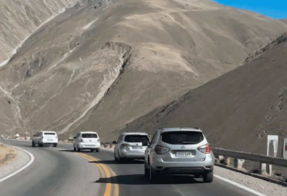 Varios autos conducen por una carretera sinuosa en los Andes peruanos, rodeados de montañas áridas y un cielo despejado. Una ruta desafiante con curvas pronunciadas.