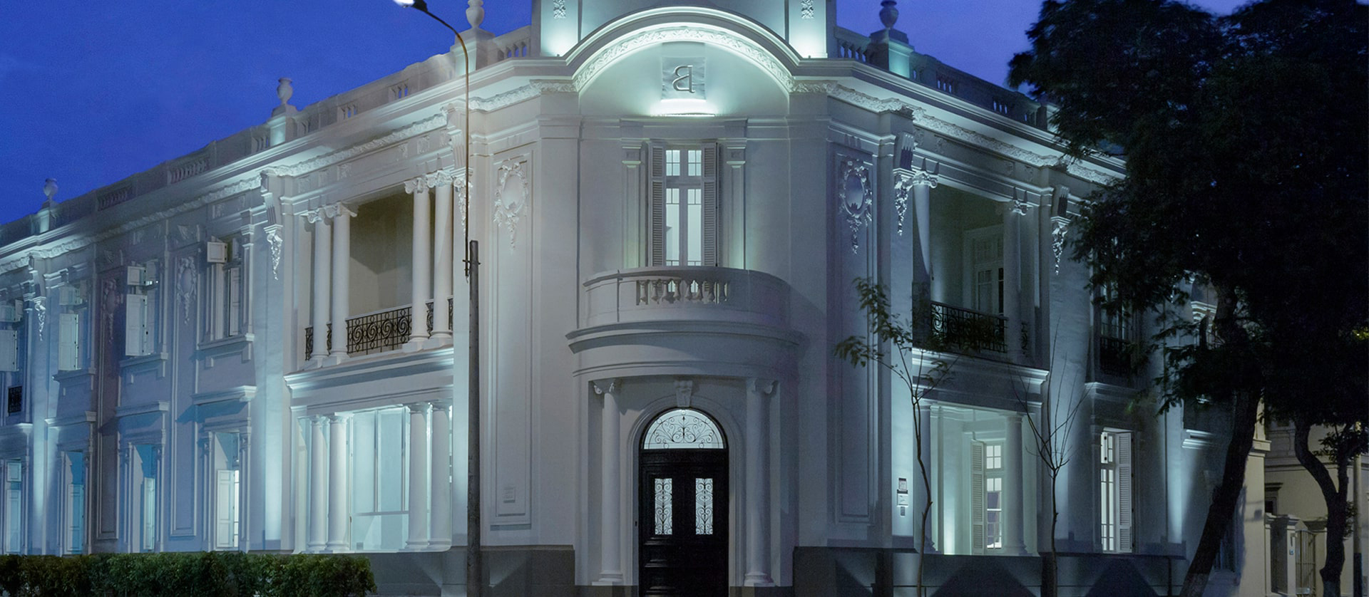 Night view of the illuminated colonial-style facade of Hotel B with balconies and columns.
