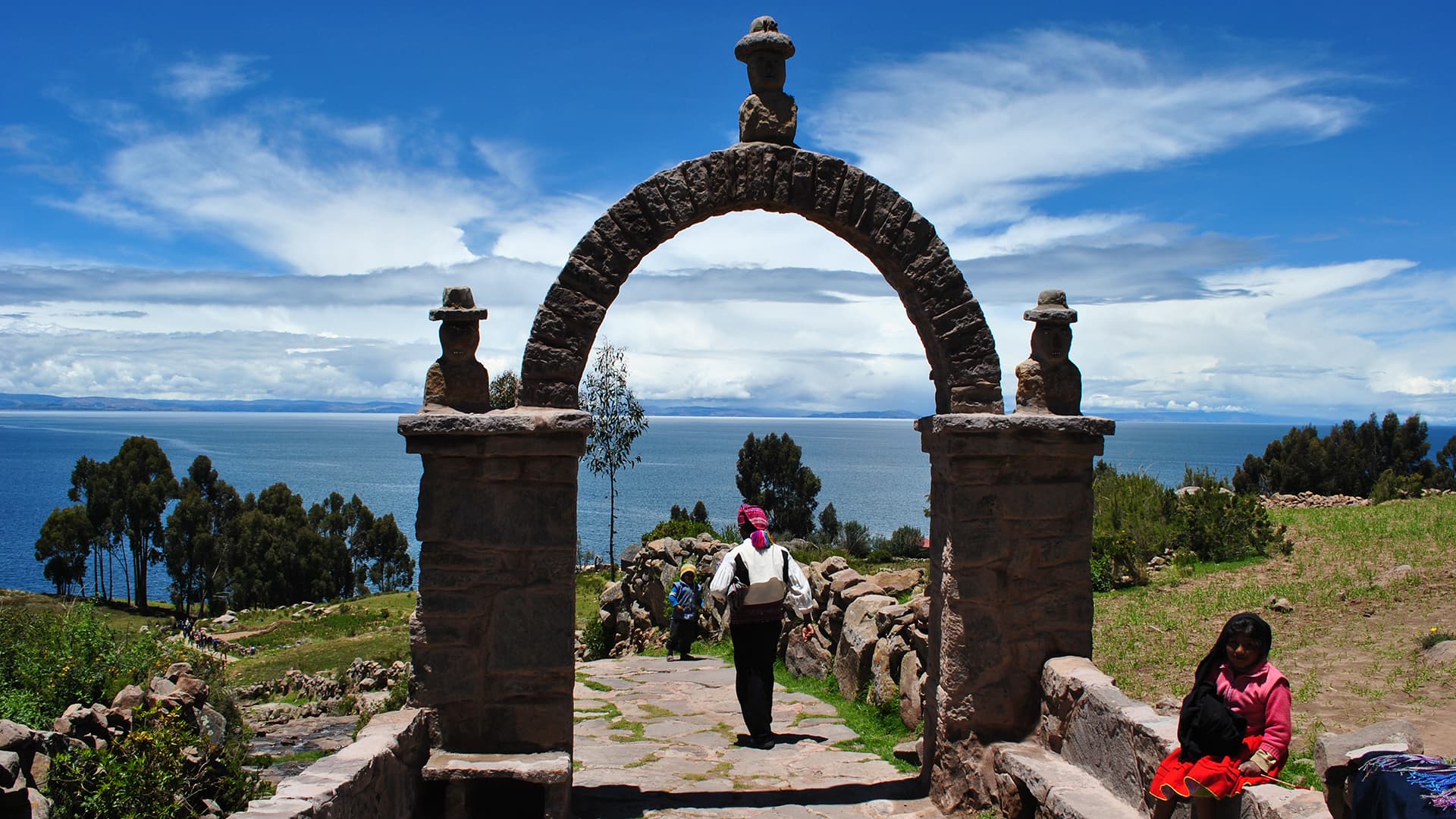 Stone arch on Isla Mantani overlooking Lake Titicaca, with people in traditional clothing.