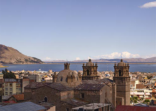 View of the Puno cityscape with colonial-style church towers and Lake Titicaca in the background.