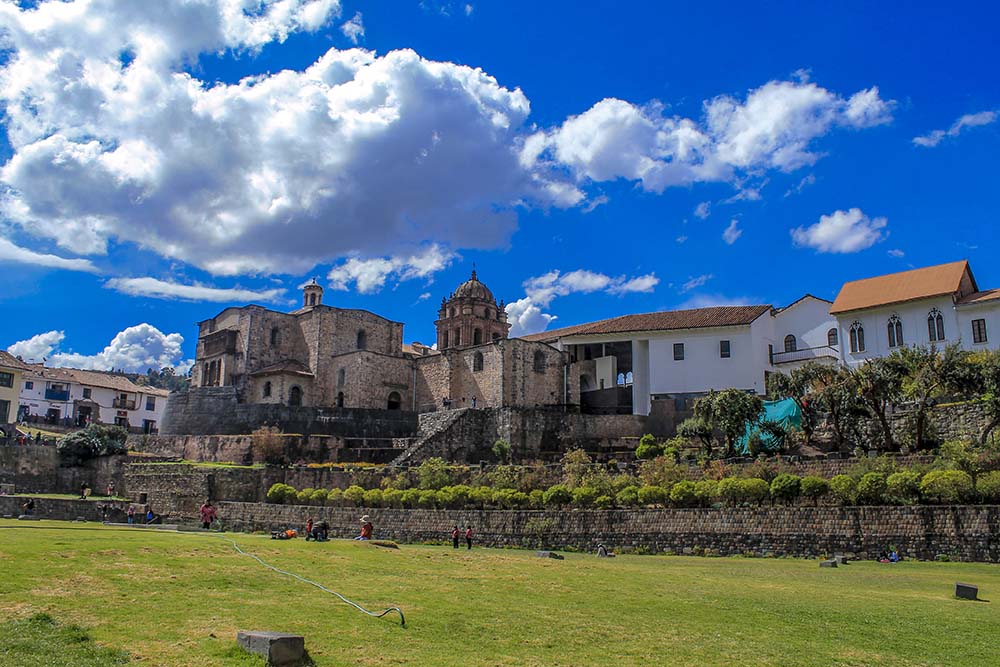 Exterior view of Qoricancha complex with colonial architecture and lush gardens under a vibrant blue sky.