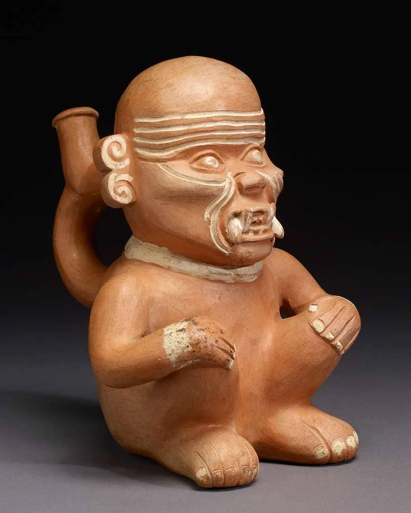 Moche ceramic sculpture depicting a seated prisoner with fangs and headband.